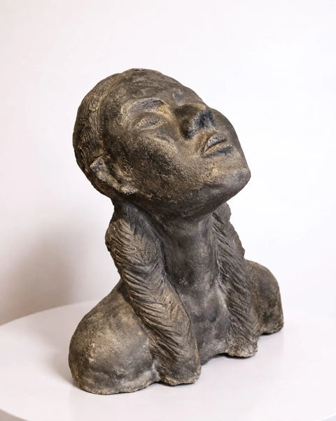 Cement portrait bust with upward-turned face and two braids, front three-quarter view